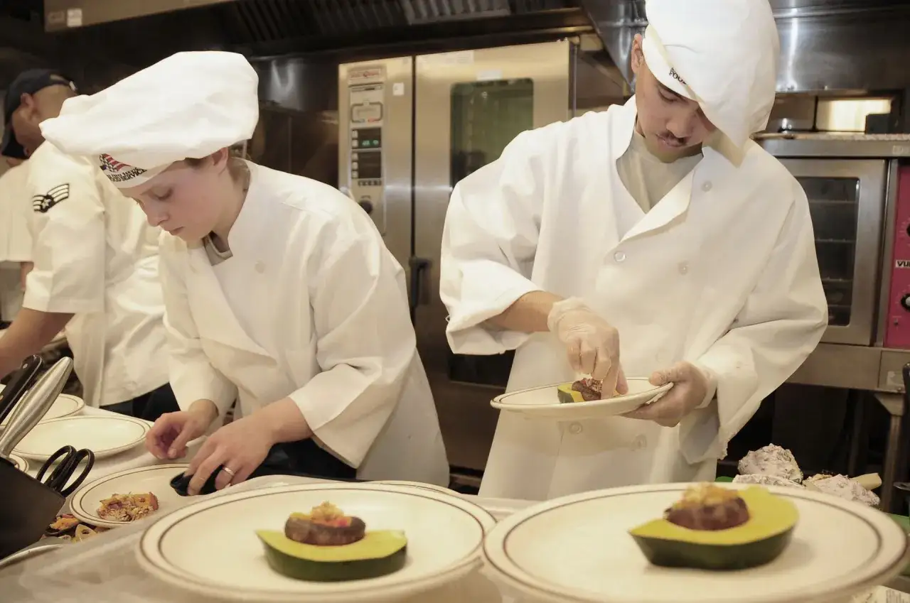 Deux chefs pr&eacute;parent des assiettes pour un contrat extra restauration. L'un d&eacute;pose une garniture sur un avocat, l'autre ajuste un plat.