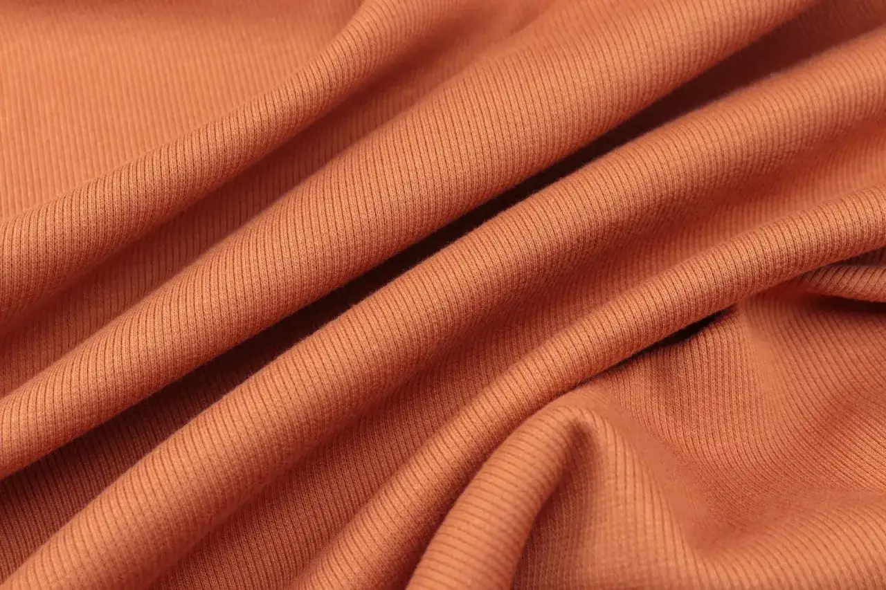 Drapé d'une matière rayonne orange, texture côtelée douce et souple, idéale pour des vêtements confortables.