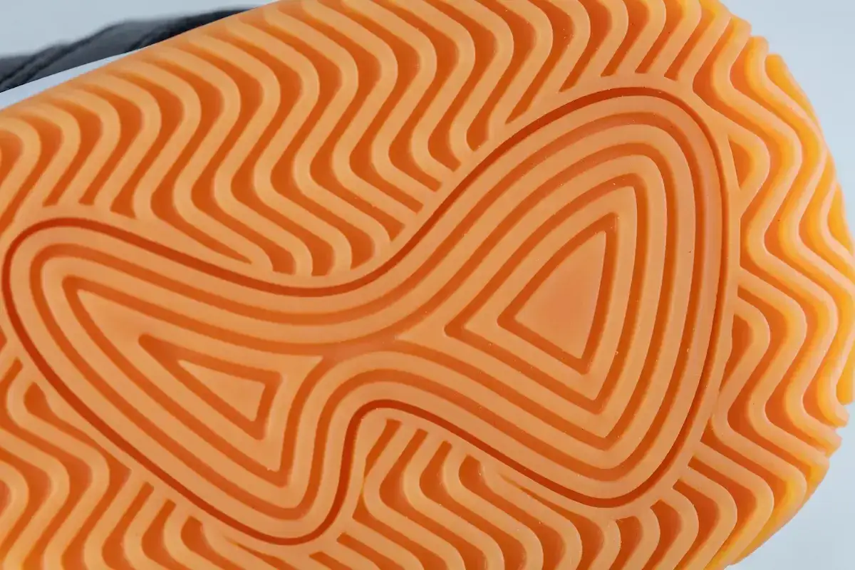 Nahaufnahme einer leuchtend orangen Schuhsohle aus Gummi oder Kunststoff mit einem wellenförmigen Profil für optimalen Halt.