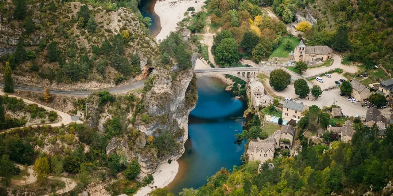 Vue aérienne des gorges du Tarn, avec un village pittoresque, un pont ancien et une rivière bleue. Une carte idéale pour planifier votre visite.