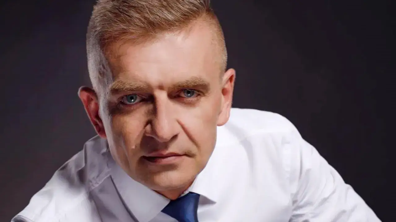 Bartosz Arłukowicz, niczym agent specjalny, w białej koszuli i granatowym krawacie, spogląda z determinacją.