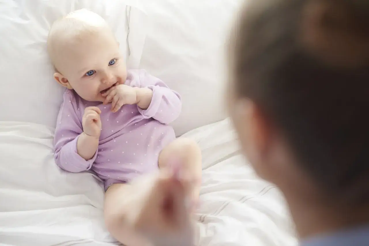 Bambino di pochi mesi, con occhi azzurri e capelli biondi, gioca con le dita. La sua lallazione &egrave; un dolce suono che annuncia la sua crescita.