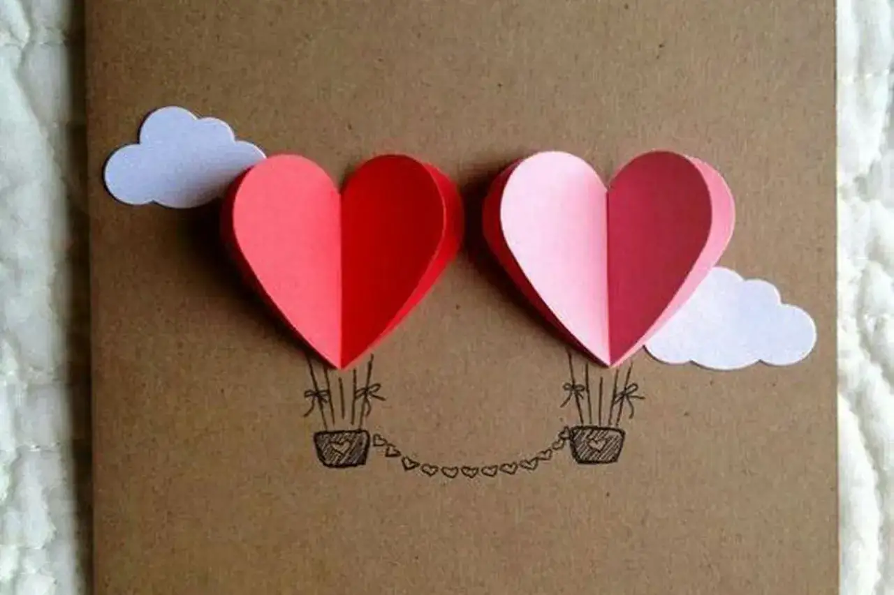 Lavoretto festa mamma: due mongolfiere a forma di cuore rosso e rosa, con nuvole bianche e cesti decorati.