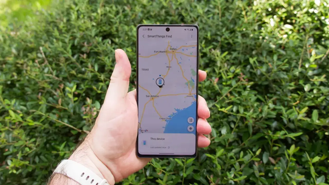 Dłoń trzyma telefon z mapą Teksasu i ikoną lokalizacji. Aplikacja SmartThings Find pokazuje, jak znaleźć telefon Samsung.
