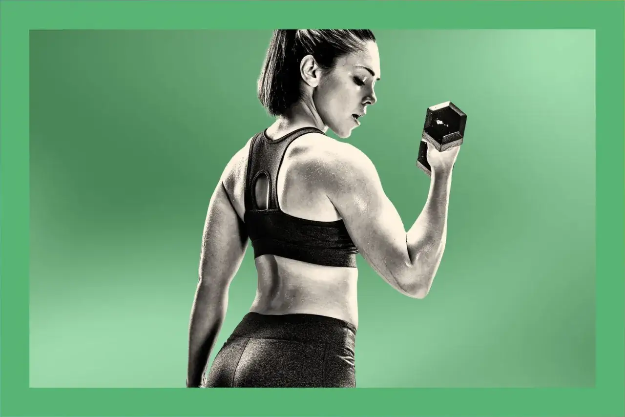 Silna fit girl ćwiczy biceps z hantlem. Jej mięśnie są napięte, a pot lśni na skórze.