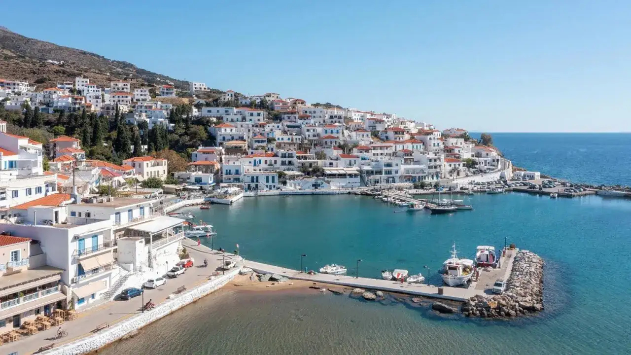 Malowniczy port na wyspie Andros, z białymi domkami pnącymi się po wzgórzu i błękitnym morzem.