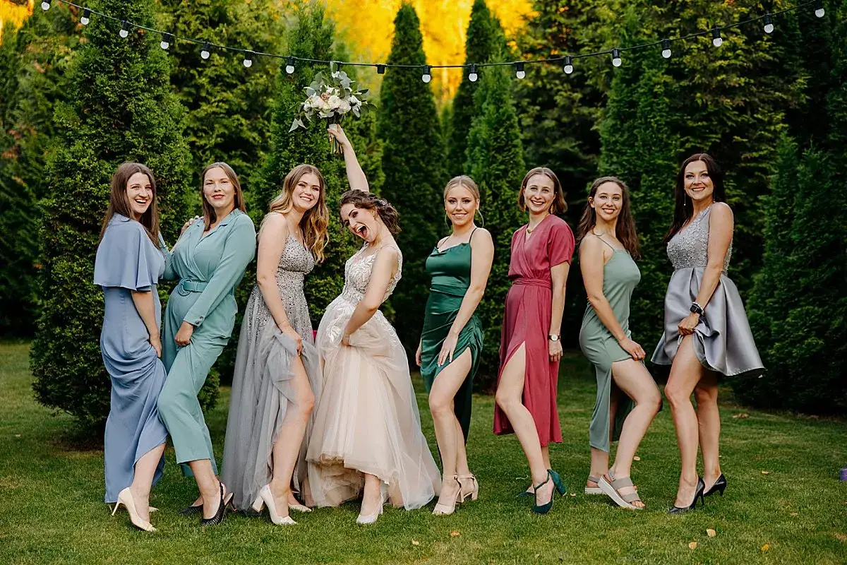 Uśmiechnięte druhny w kolorowych sukniach, gotowe na profilowe na grupę. Panna młoda z bukietem w górze.