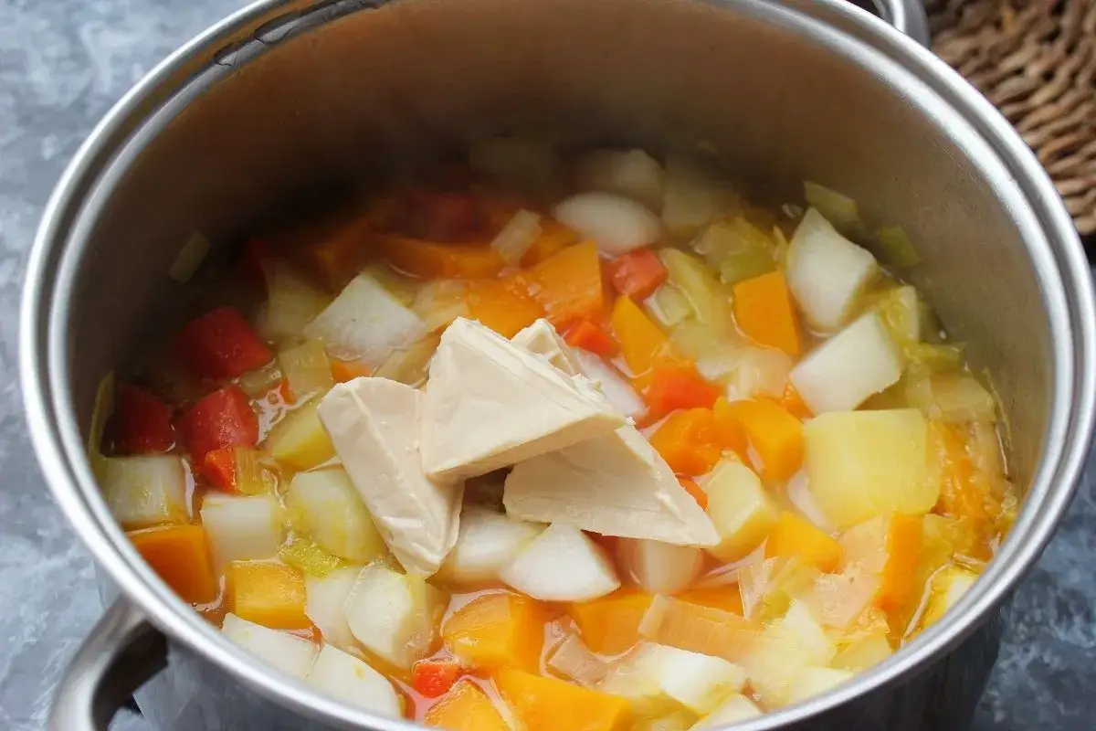 Trozo de tofu en una olla con verduras cortadas, como zanahoria y patata, para espesar un pur&eacute;.
