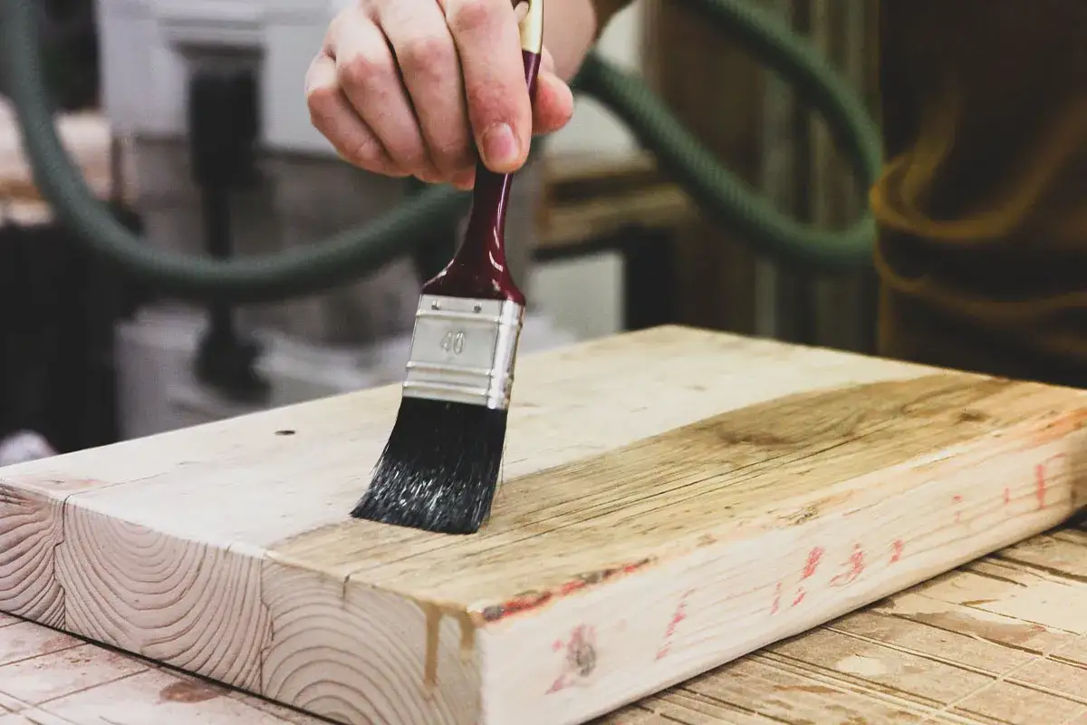 Mano che applica vernice trasparente per verniciare legno grezzo abete.