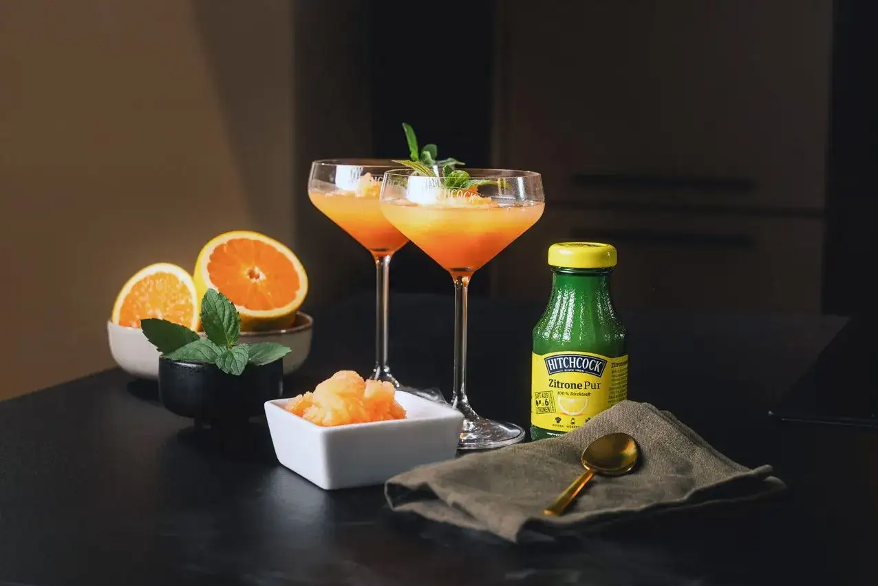 Zwei Aperol Spritz Cocktails mit Orangen und Minze, dazu ein Schälchen mit Aperol Eis.