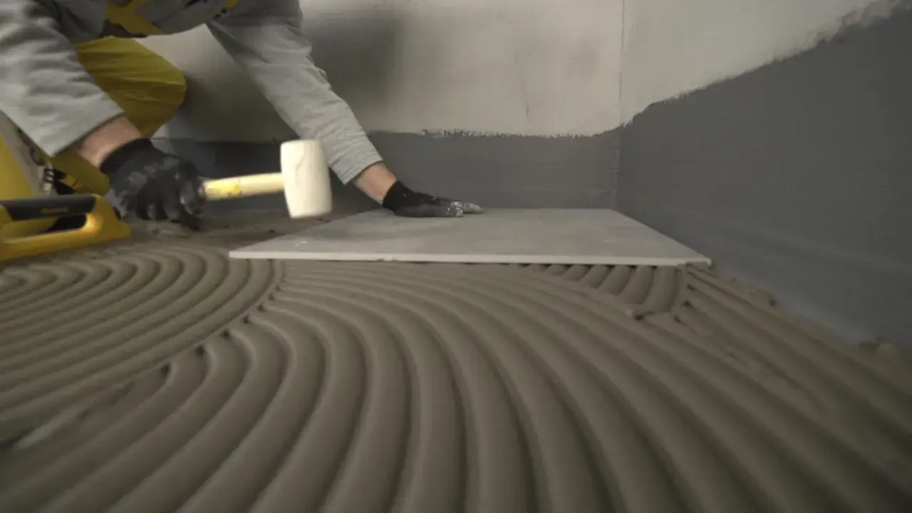 Pose d'une nouvelle dalle de carrelage sur un lit de colle fraîche, avant le séchage du carrelage. Un maillet en caoutchouc est utilisé pour ajuster la pose.