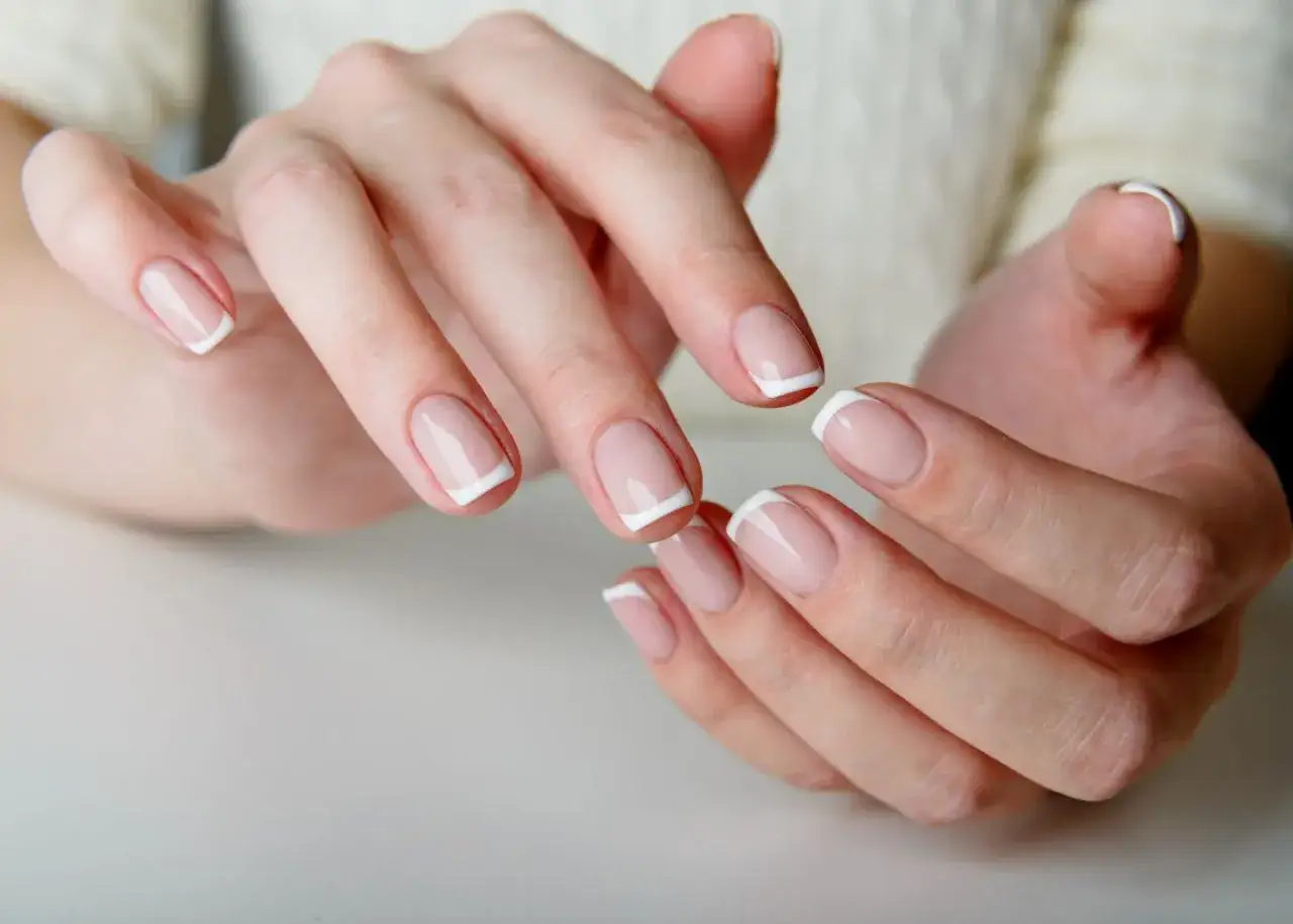 Mains aux ongles parfaits, une illustration de comment faire une french manucure. Lignes blanches nettes sur base nude.
