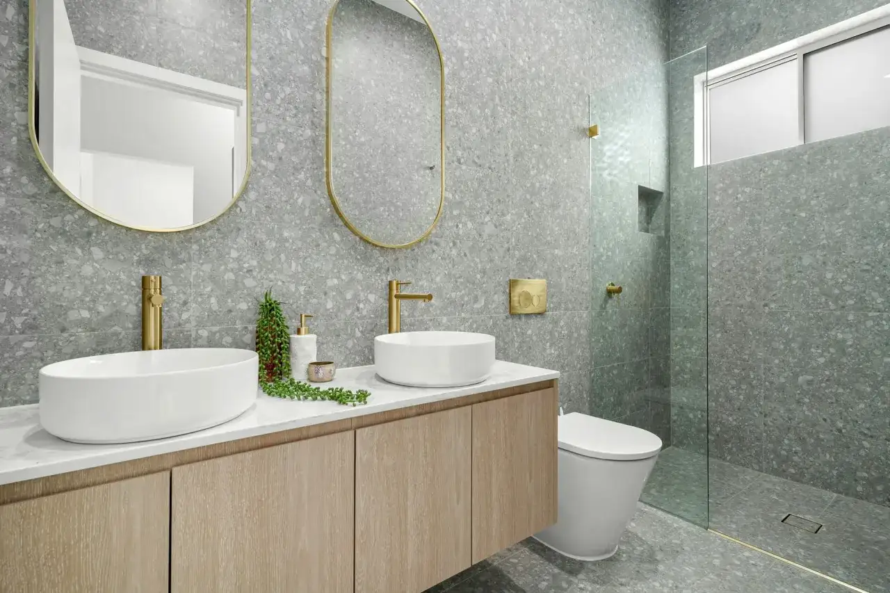 Elegante decoracion baños con lavabos blancos, grifería dorada y azulejos de terrazo gris.