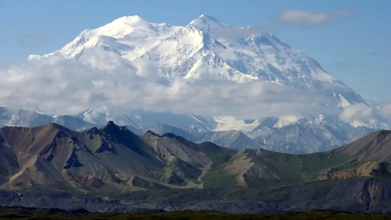 Majestatyczny, ośnieżony najwyższy szczyt Ameryki Północnej, Denali, góruje nad skalistymi, zielonymi przedgórzami.