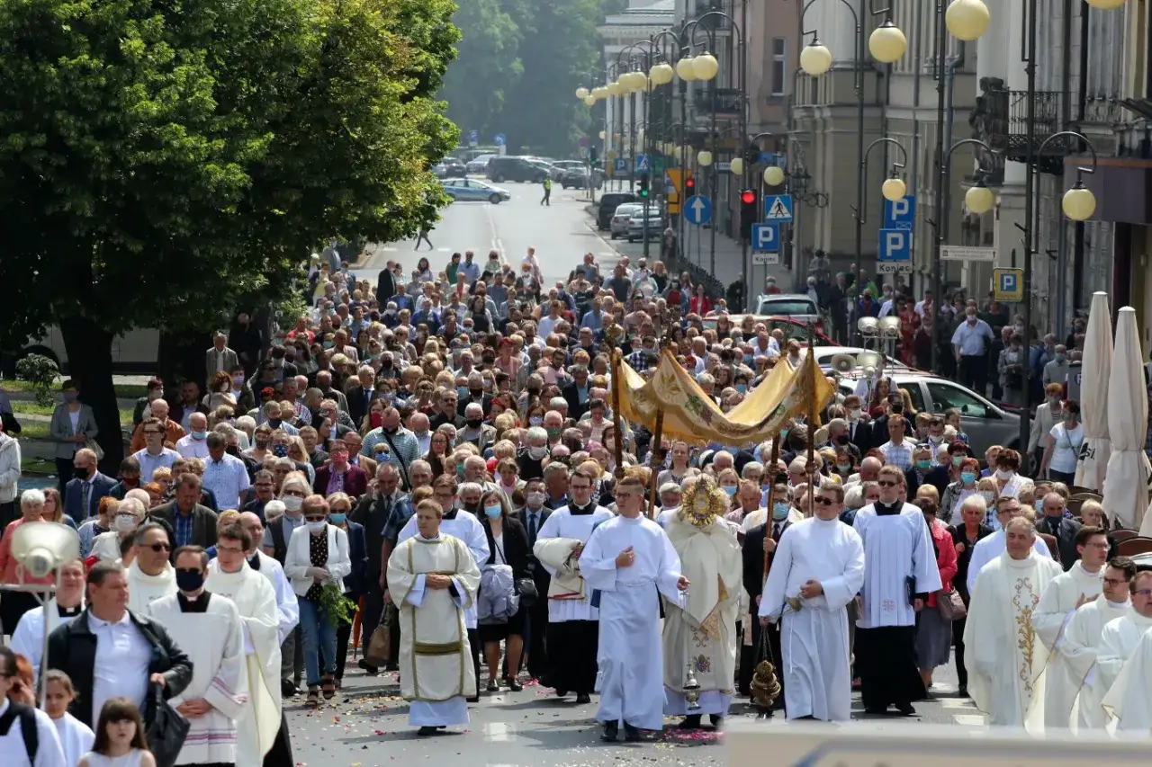 Tłum wiernych idzie ulicą w procesji. Wśród nich duchowni niosą baldachim i monstrancję. To wyjątkowe **święta w czerwcu**.
