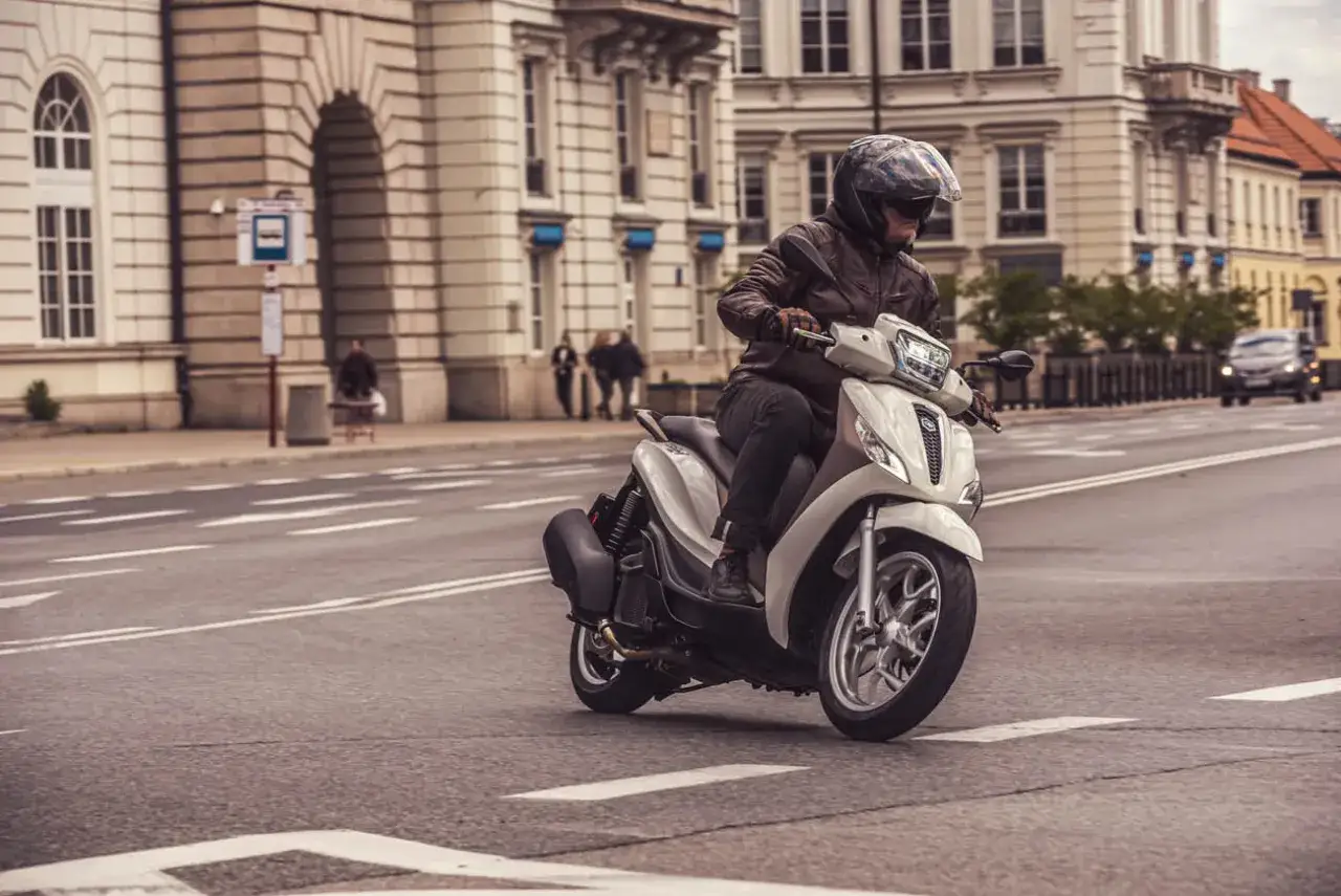 Mężczyzna w kasku i skórzanej kurtce jedzie skuterem Piaggio Medley po miejskiej ulicy.