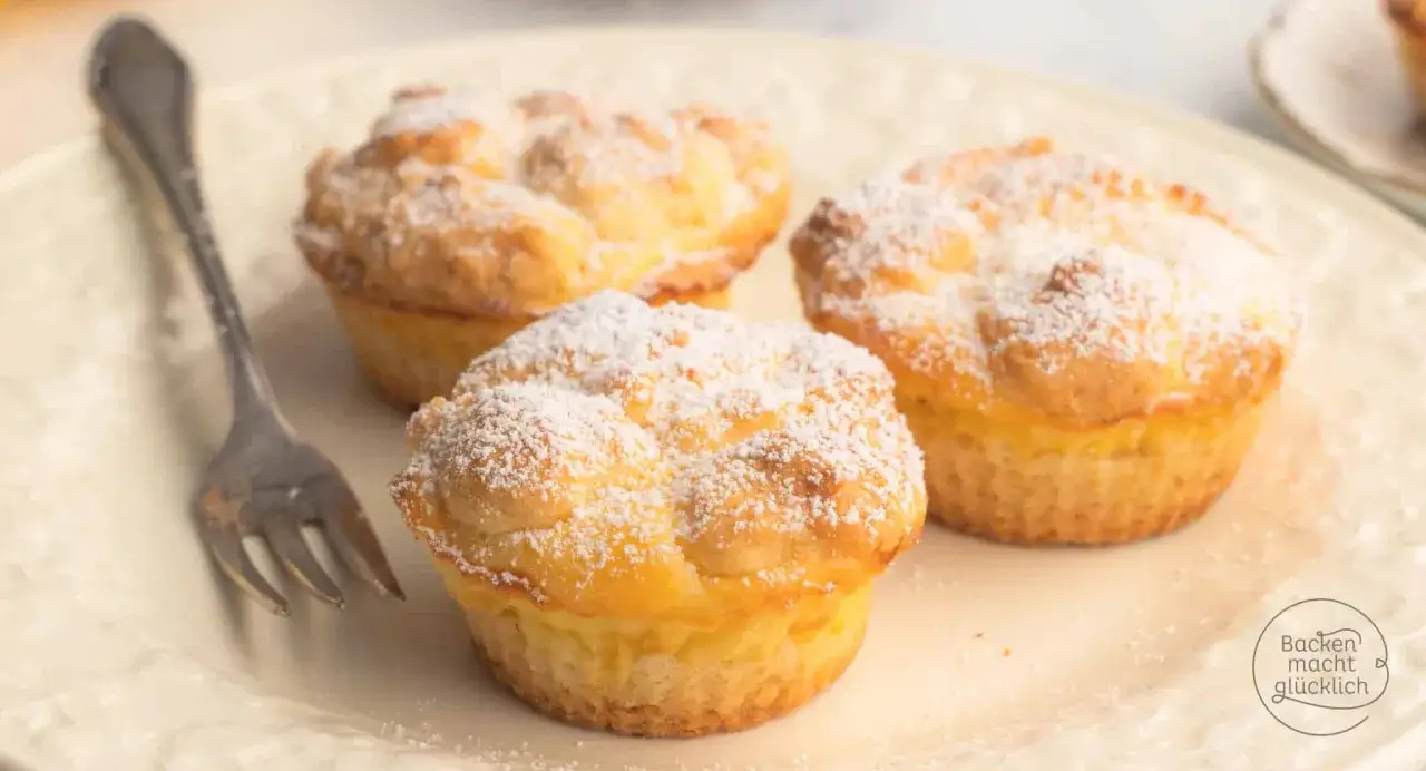 Drei luftige Cheesecake Muffins, mit Puderzucker bestäubt, auf einem Teller mit einer Gabel.