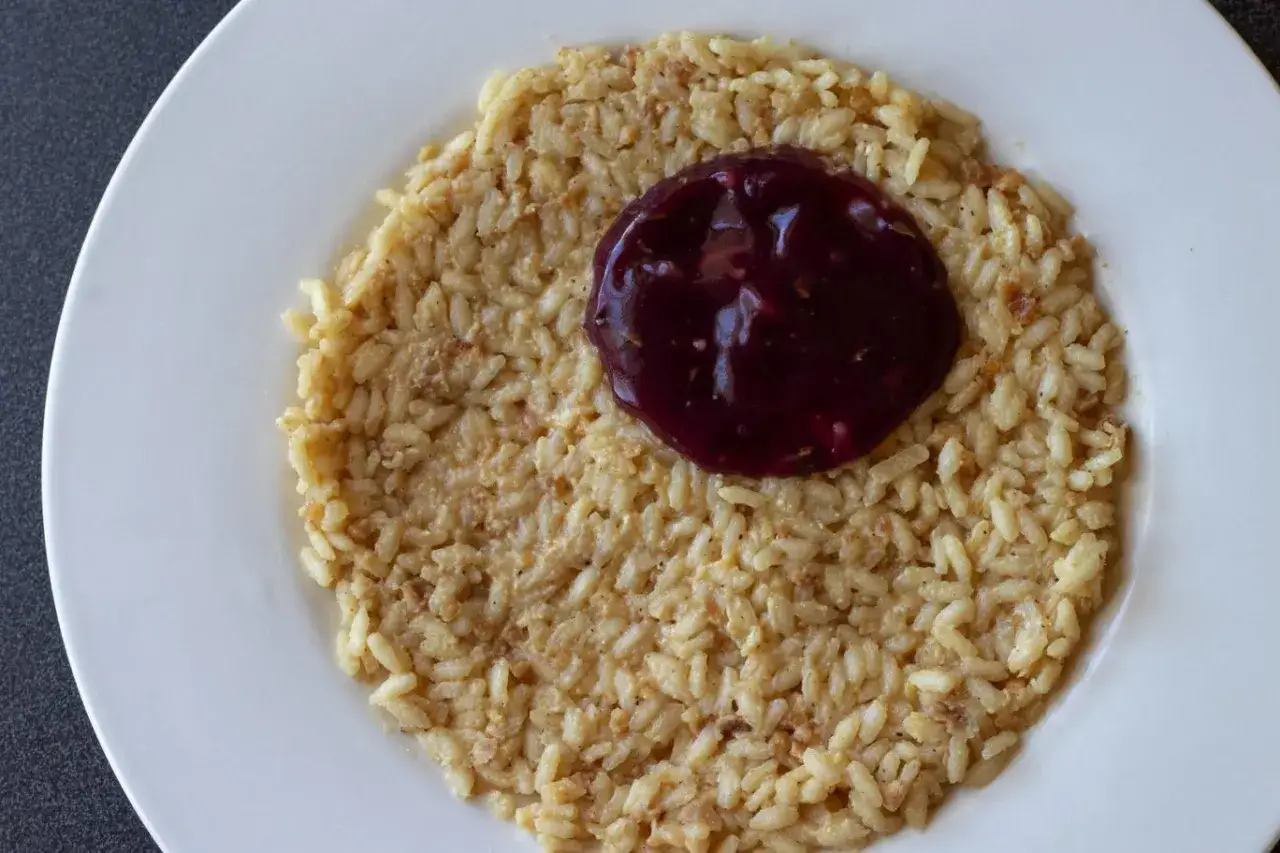 Un cremoso risotto al porto, arricchito da una salsa scura e lucida, servito su un piatto bianco.