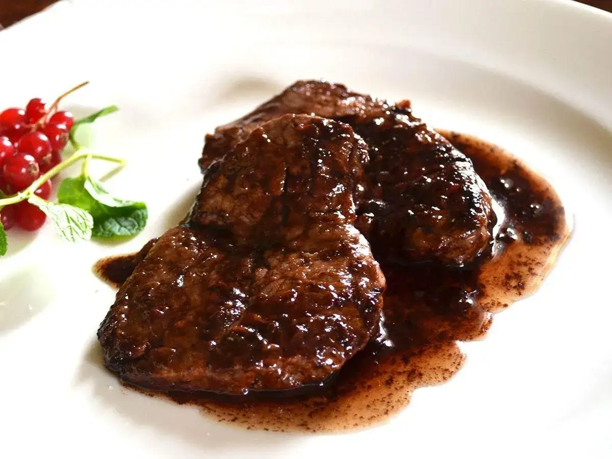 Succulento stracotto al Chianti, servito su un piatto bianco con ribes rossi e menta fresca.