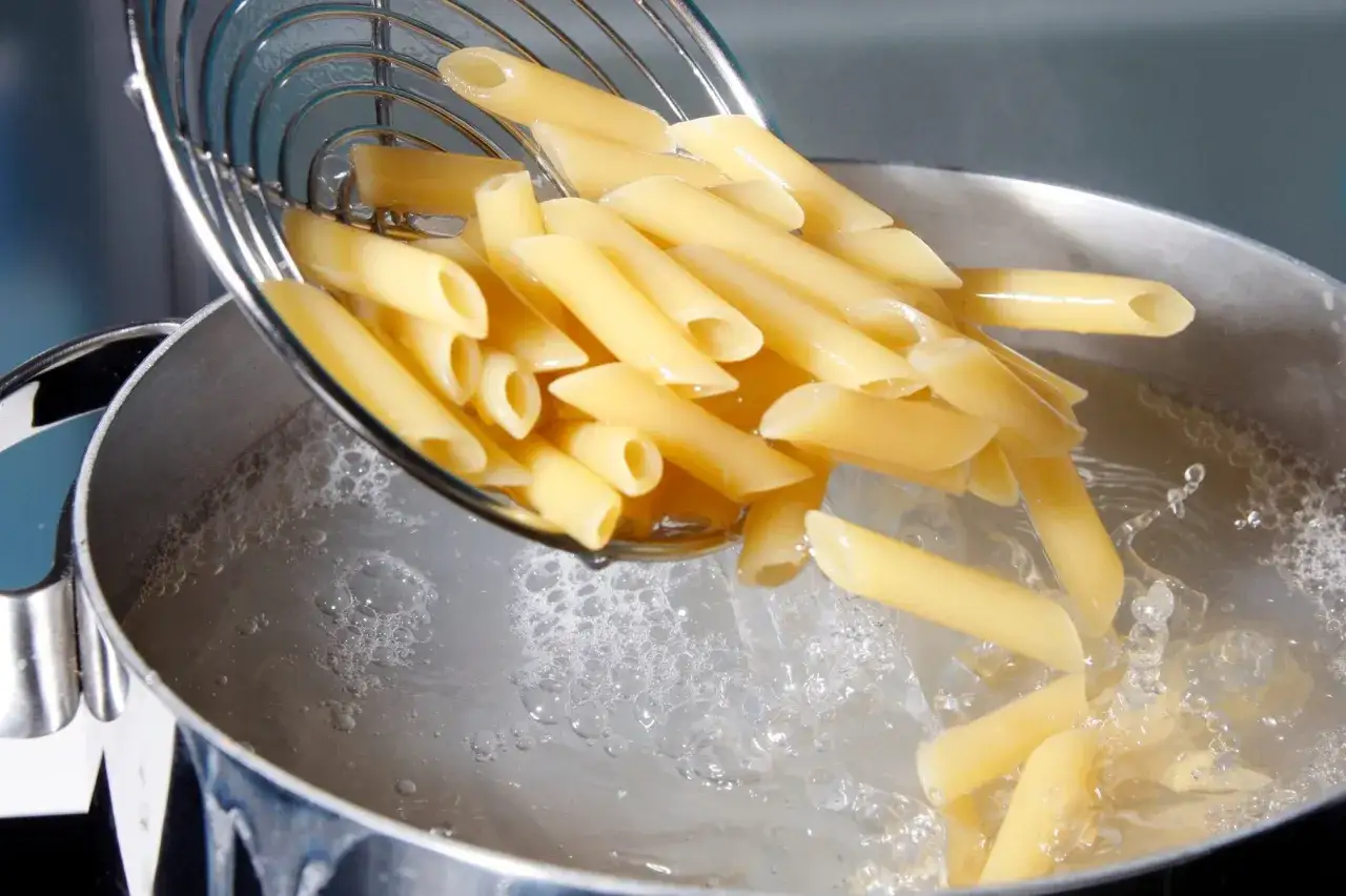 Pâtes penne tombant dans l'eau bouillante pour la cuisson. Le bruit de l'eau qui éclabousse annonce le début du repas.