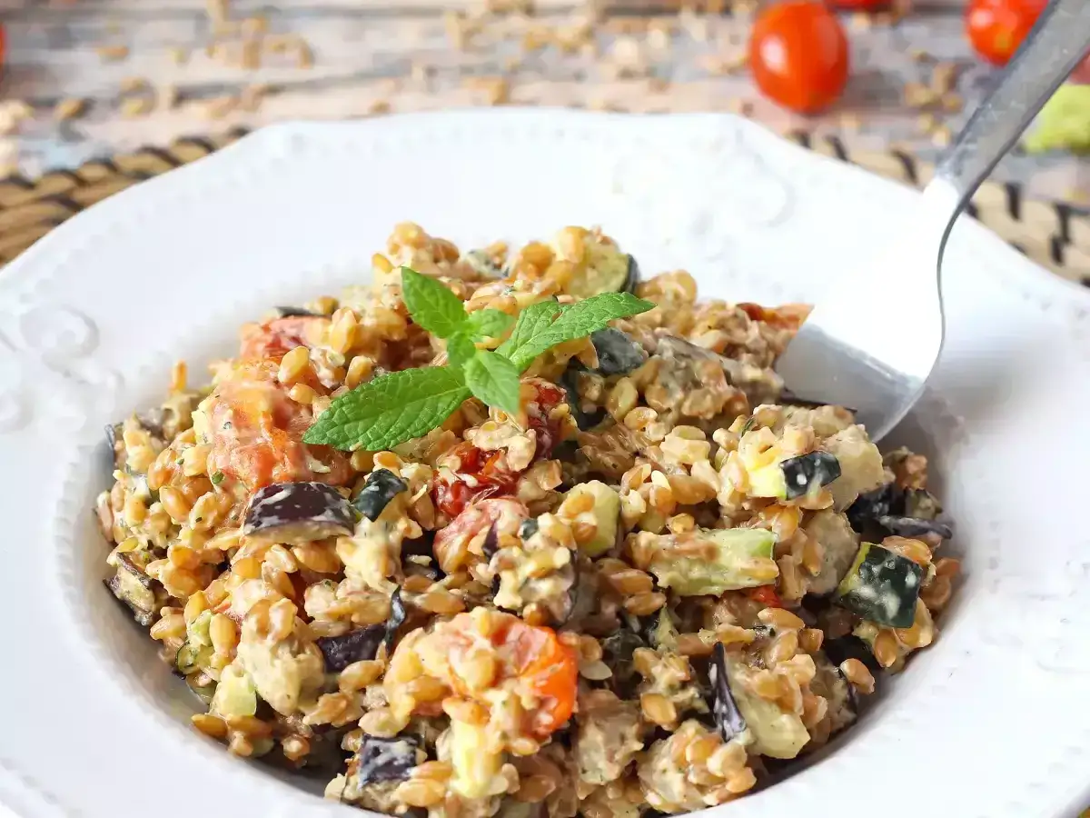 Un'appetitosa insalata di farro con verdure miste, pomodorini e una fogliolina di menta fresca.