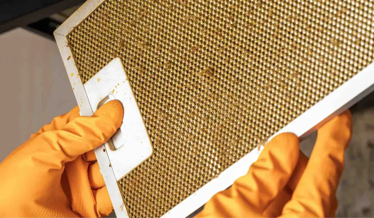 Mani con guanti arancioni tengono un filtro della cappa della cucina sporco, pronto per essere pulito.