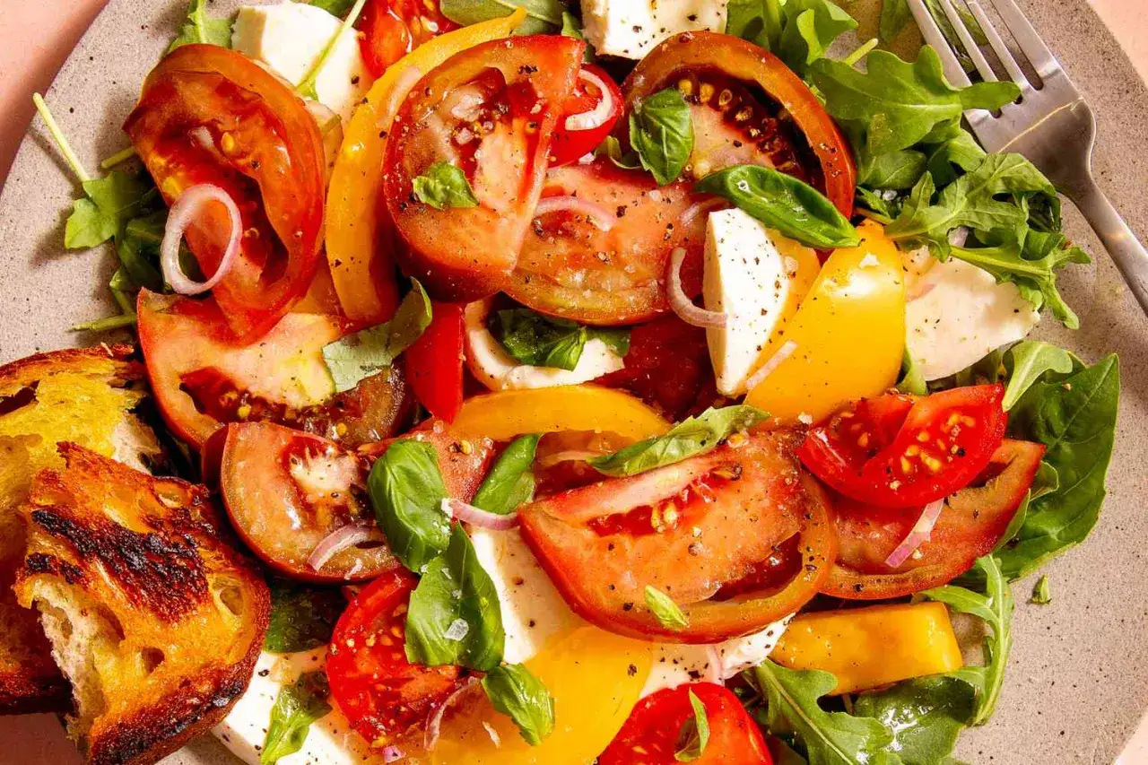 Ensalada caprese vibrante con tomates, mozzarella fresca, albahaca y pan tostado.