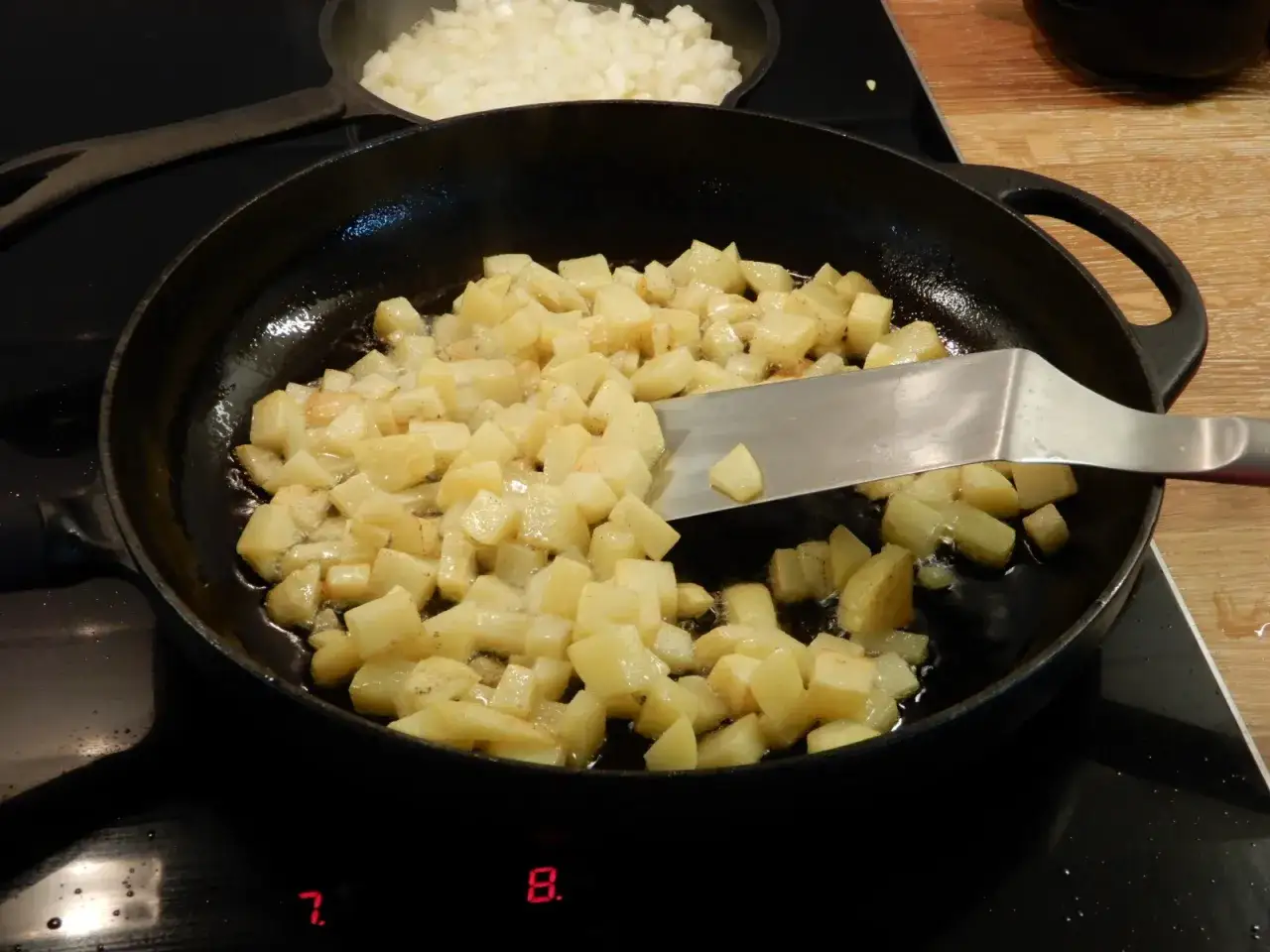 Råstekt potatis fräser i en gjutjärnspanna. En stekspade vänder på de gyllene bitarna.