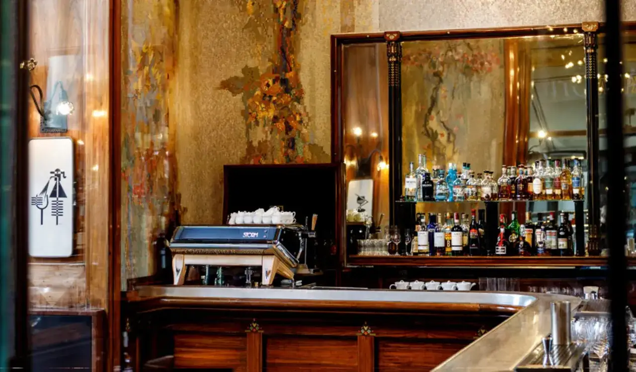 Un elegante caffè illuminismo con un bancone in legno scuro, una macchina per caffè e bottiglie di liquore su uno scaffale riflettente.