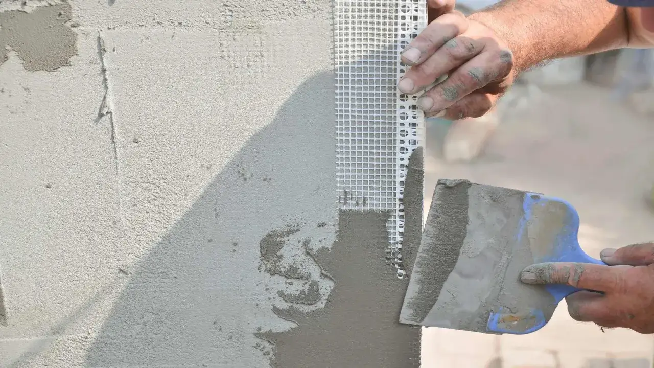 Mani esperte applicano intonaco su rete per come riparare un muro. La spatola stende il materiale con precisione.