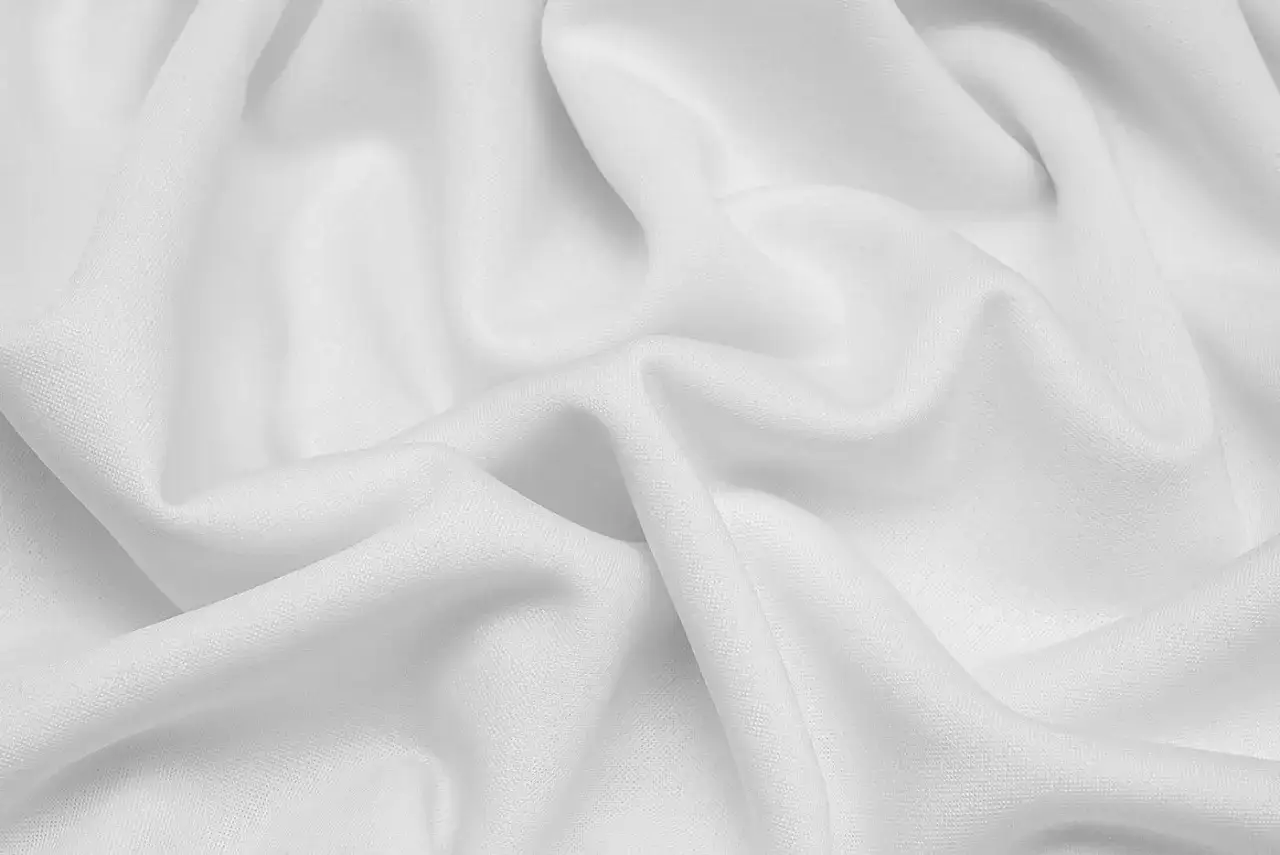 Gładka, biała dzianina nurek układa się w miękkie fale, tworząc wrażenie lekkości i elegancji.