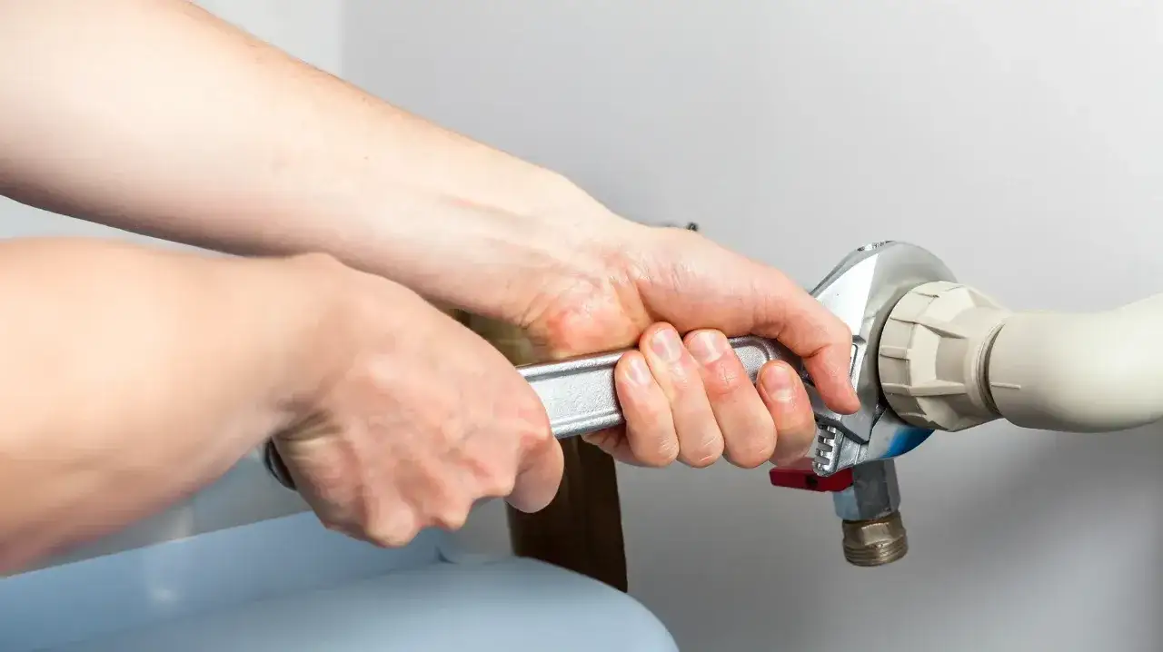 Mains d'un plombier serrant un raccord avec une cl&eacute; pour r&eacute;parer un probl&egrave;me o&ugrave; mon adoucisseur coule en permanence.