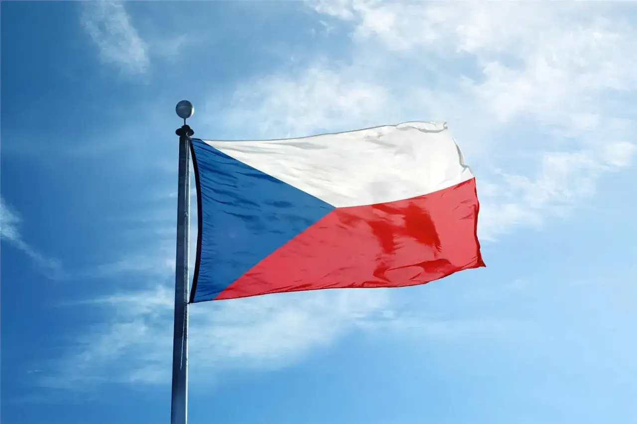 Flaga Czech powiewa na tle błękitnego nieba z białymi chmurkami.