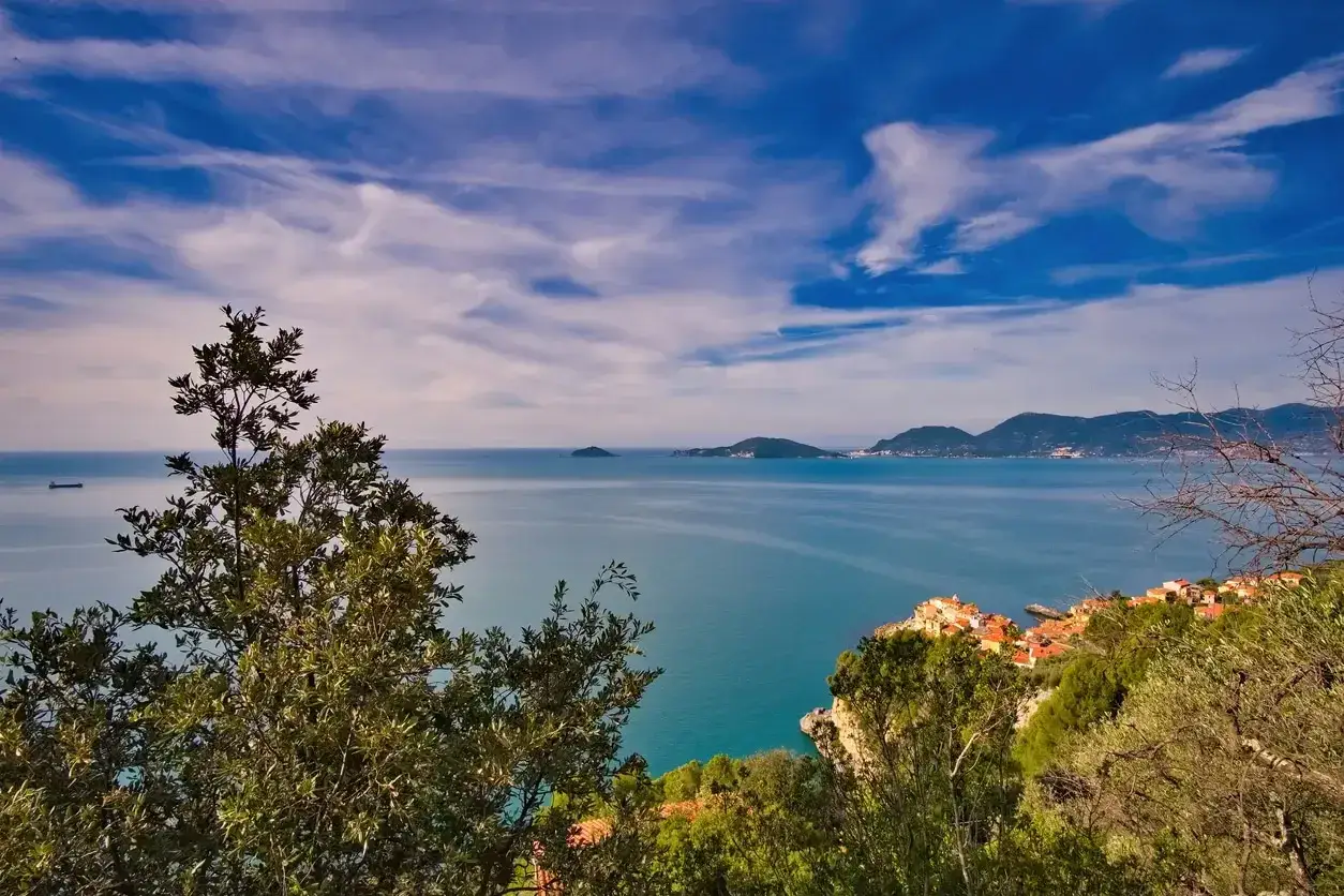 Vista panoramica sul mare blu della Liguria, con un villaggio costiero e montagne sullo sfondo. Perfetto per i cammini in Liguria.