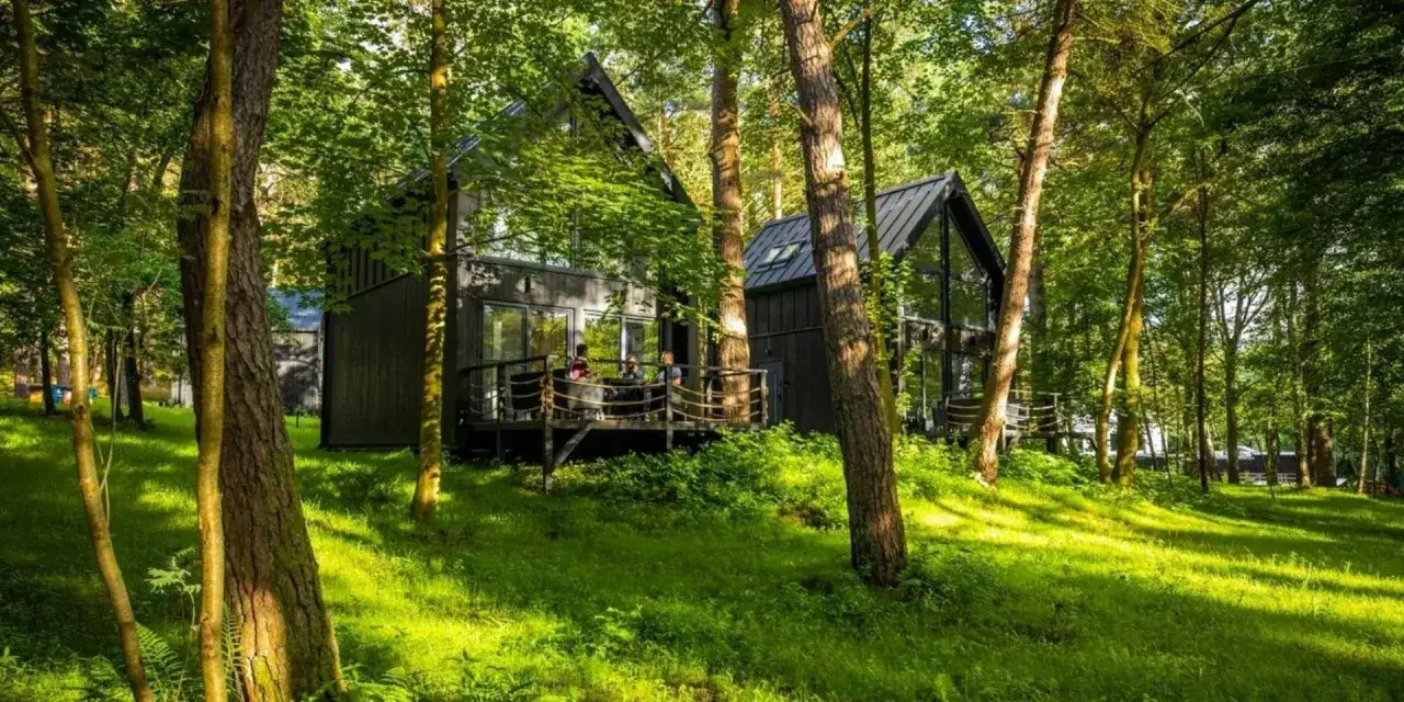 Nowoczesny hotel w lesie, z drewnianym tarasem i ludźmi relaksującymi się wśród drzew.