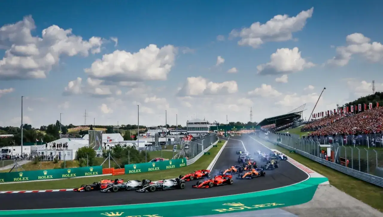 Coches de F1 en plena acci&oacute;n durante los entrenamientos libres del GP de Hungr&iacute;a. El p&uacute;blico llena las gradas bajo un cielo azul con nubes.