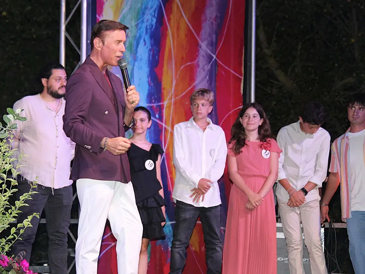 Presentazione di giovani cantanti marchigiani sul palco, con un presentatore che parla al microfono.