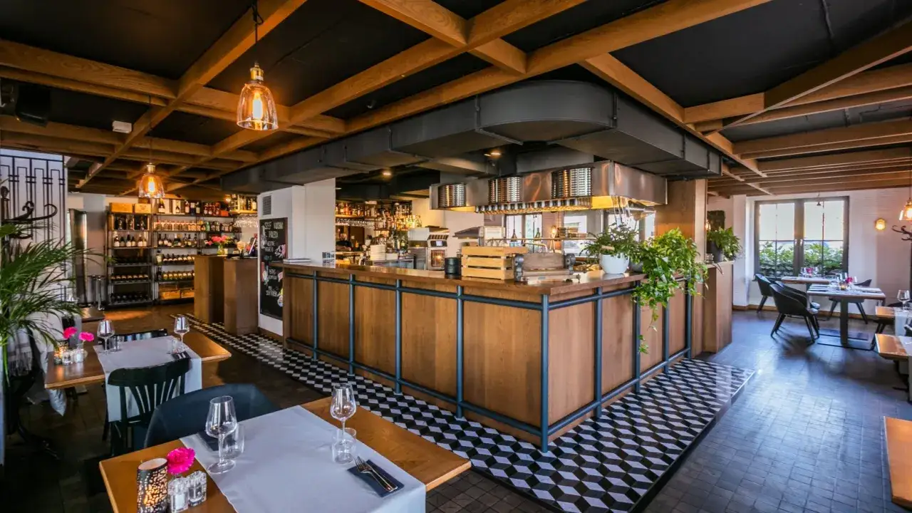 Wnętrze restauracji Magiel: drewniany bar, regały z winami, stoły z nakryciami i stylowe oświetlenie tworzą przytulną atmosferę.