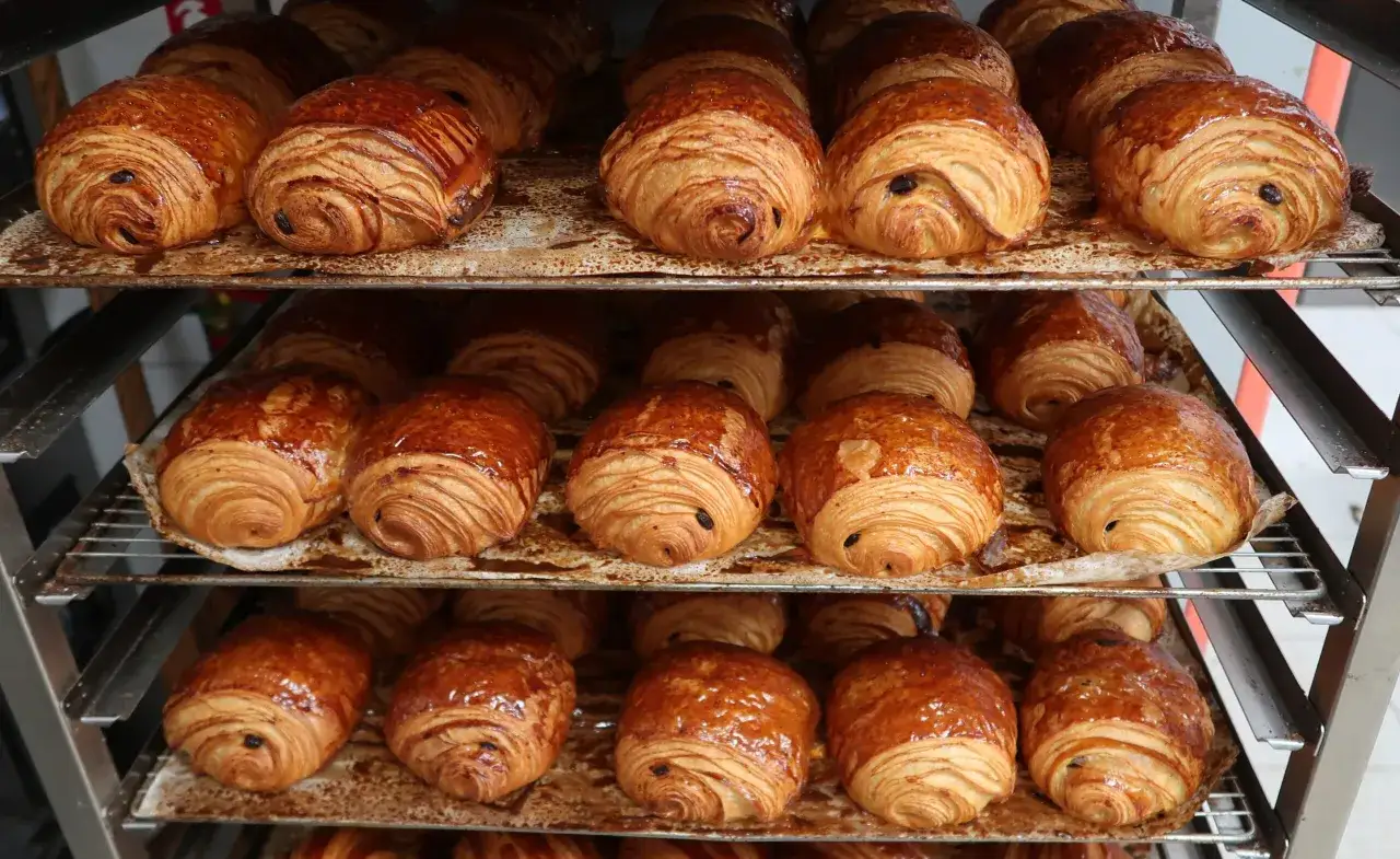 Des pains au chocolat dor&eacute;s et brillants, pr&ecirc;ts &agrave; &ecirc;tre d&eacute;gust&eacute;s, empil&eacute;s sur des grilles.