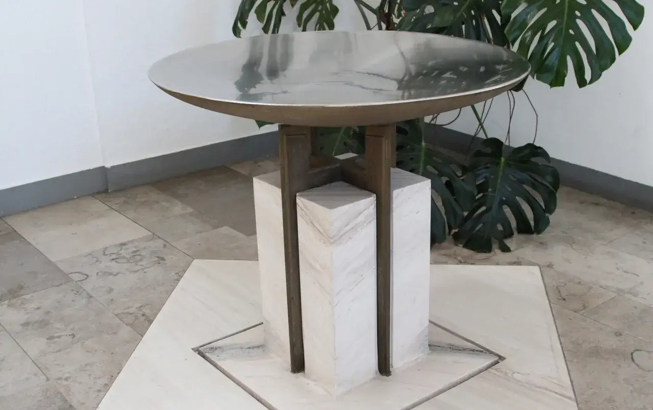 Moderner Altar in einem katholischen Kircheninnenraum, mit einer runden Metallplatte auf einem Marmorsockel, umgeben von Pflanzen.