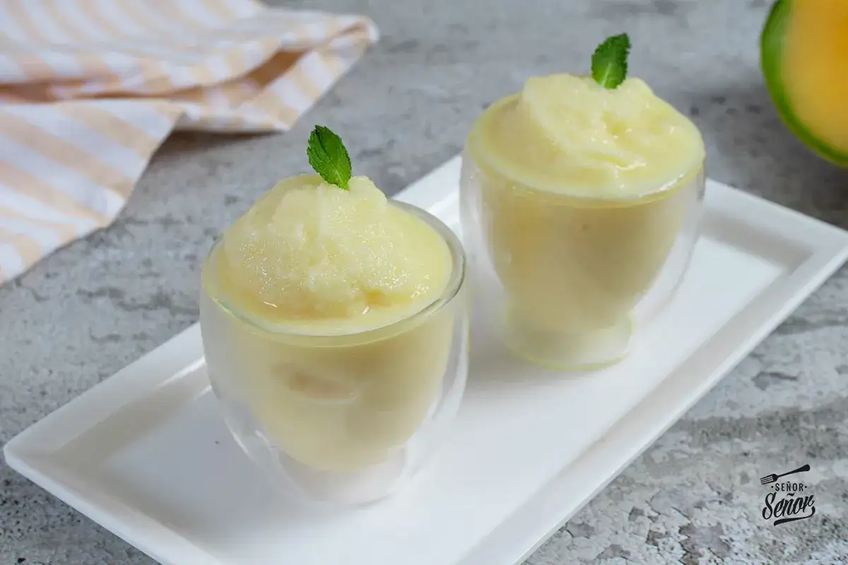 Dos copas de refrescante sorbete de melón, decoradas con hojas de menta, listas para disfrutar en un día caluroso.