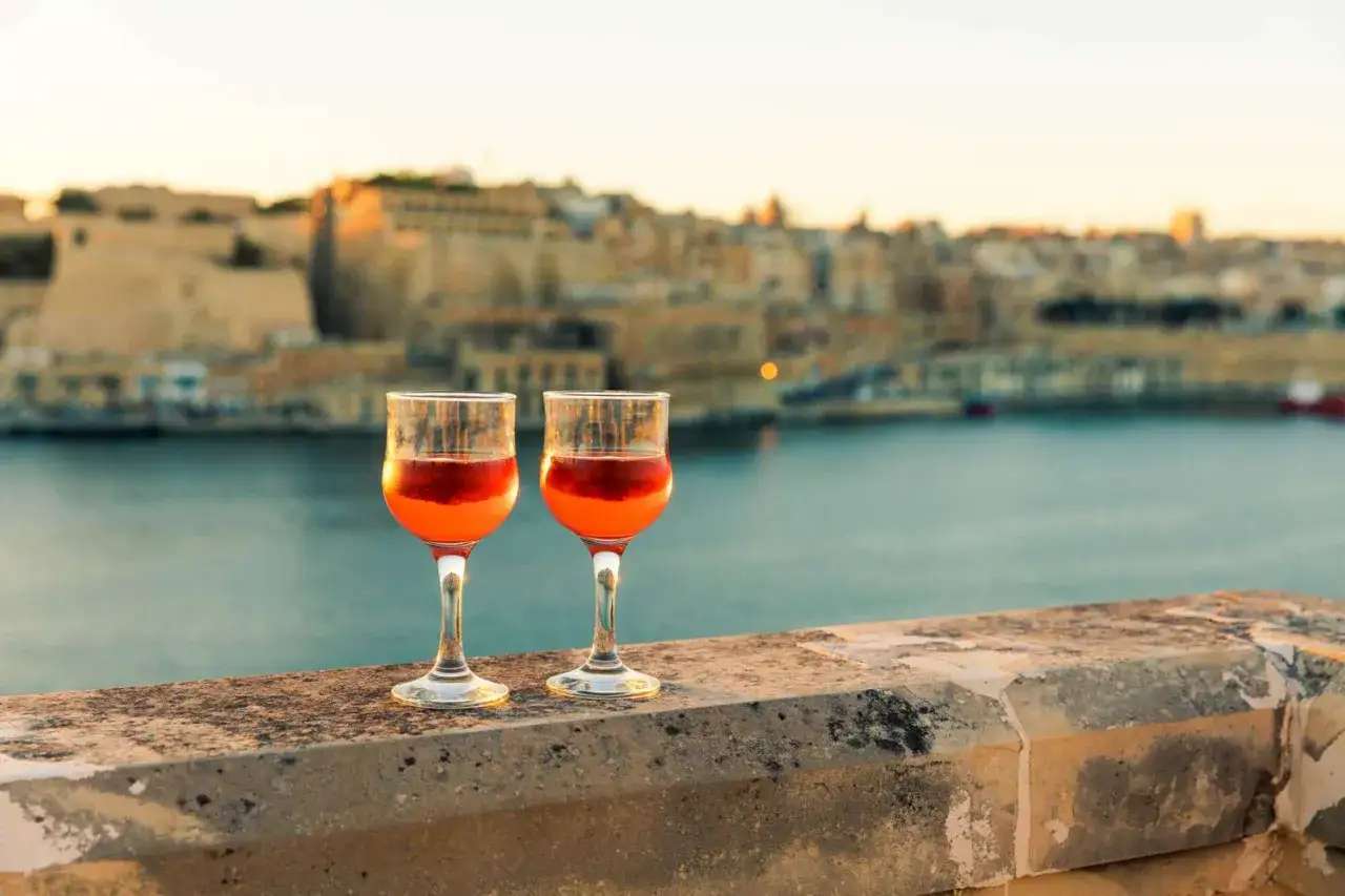 Dwa kieliszki z drinkami na tle maltańskiego krajobrazu. Idealny moment na relaks z drinkiem i podziwianie widoków. Malta alkohol.