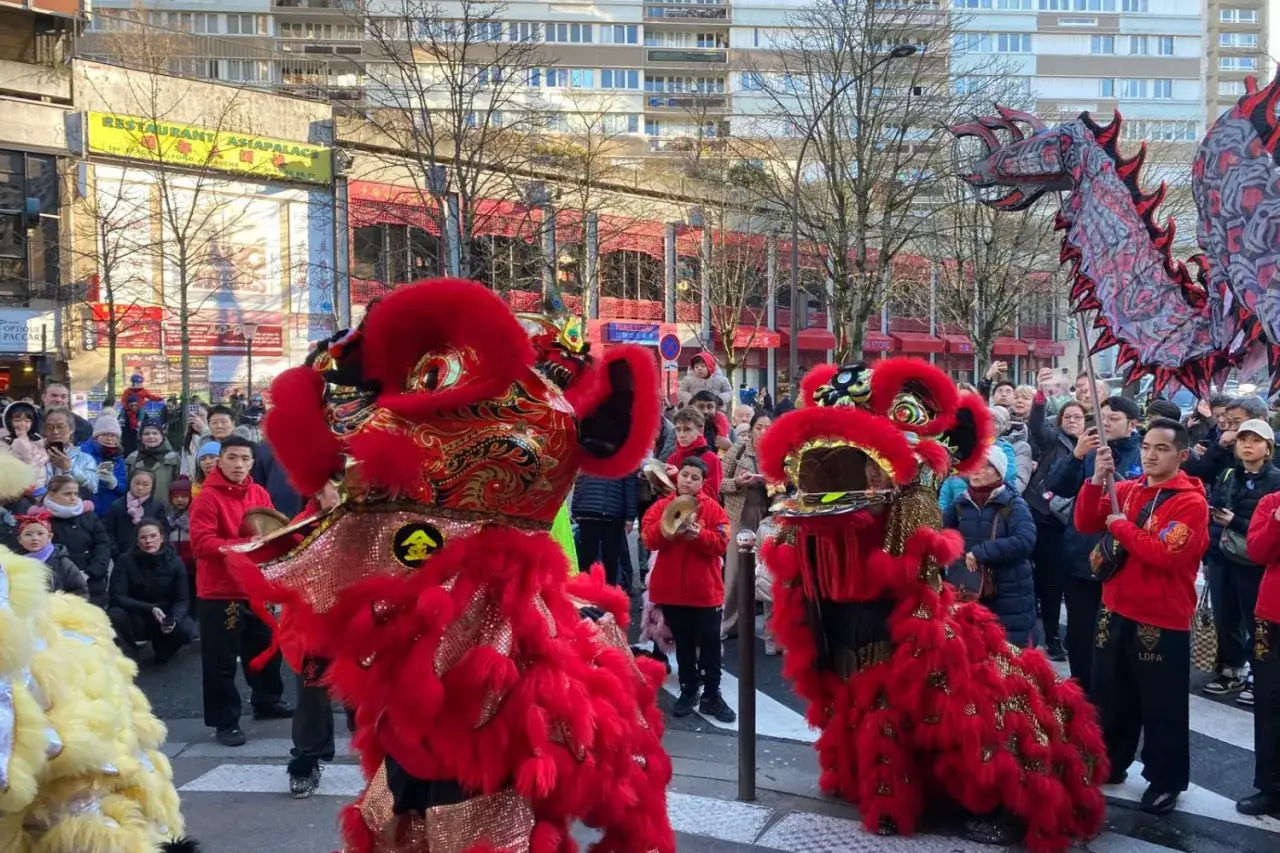 Danse des lions rouges et d'un dragon lors d'un défilé du nouvel an chinois, sous les regards d'une foule joyeuse.