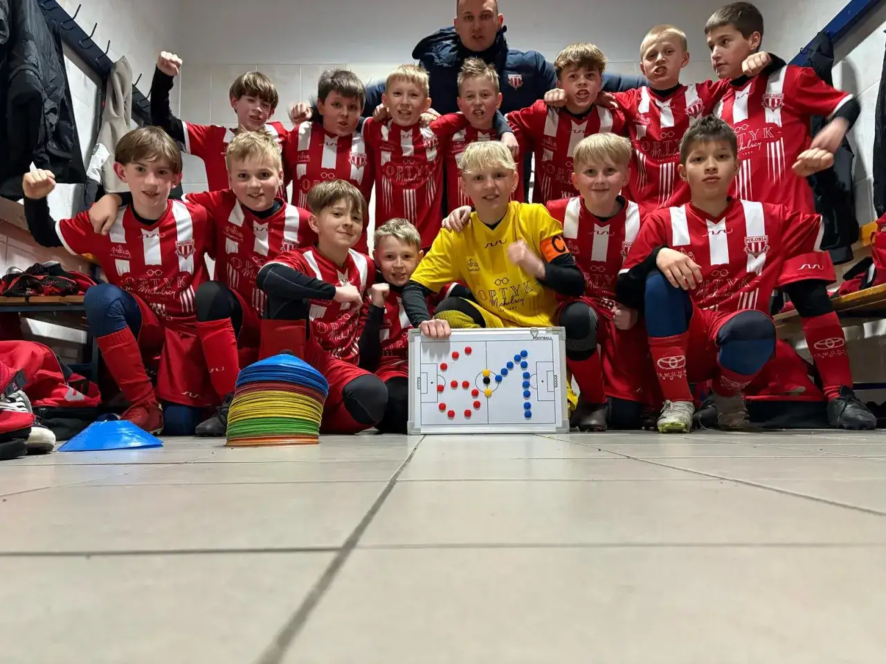 Młodzi piłkarze w czerwonych strojach z trenerem, gotowi do gry. To może być najmłodszy klub piłkarski na świecie, pełen pasji i determinacji.