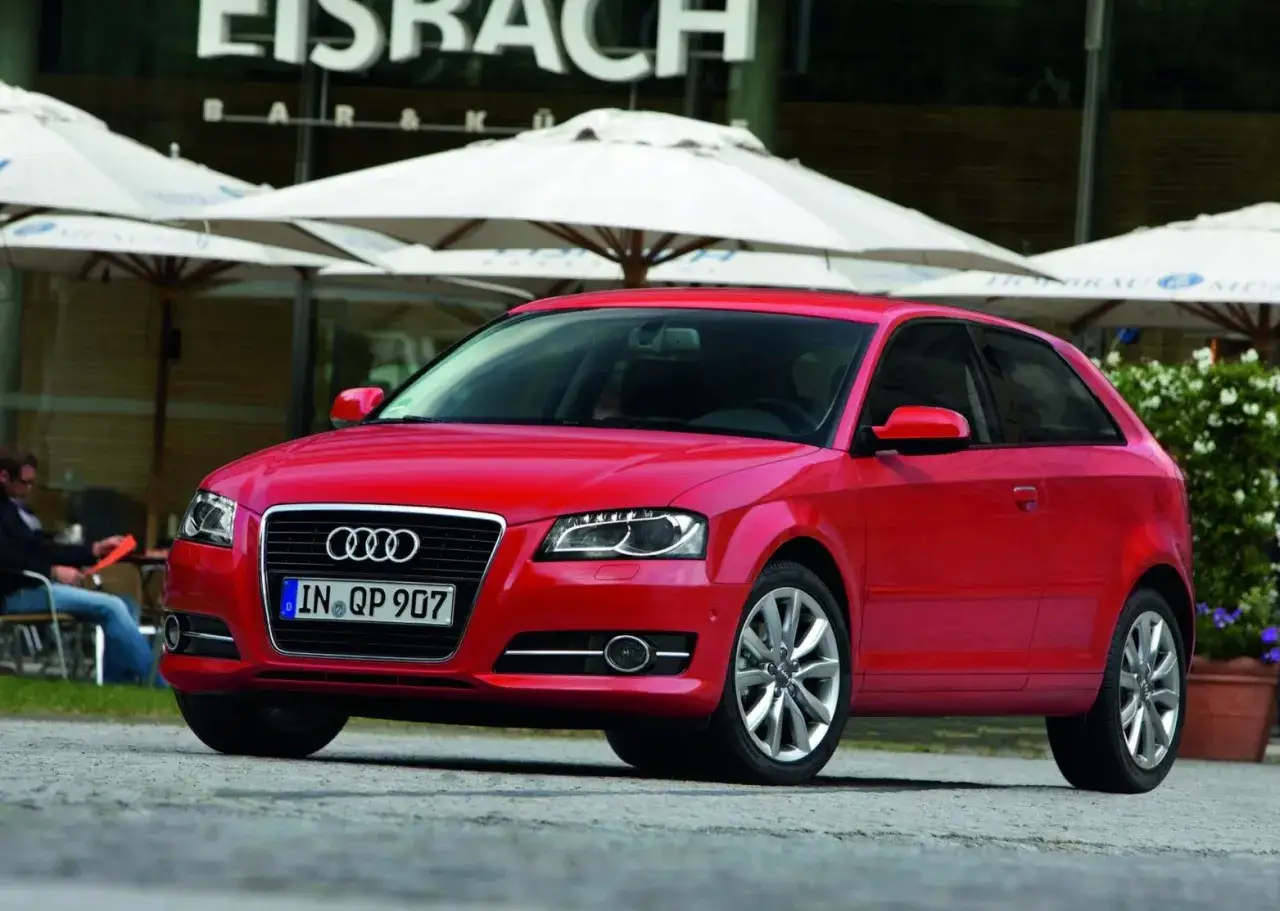 Roter Audi A3 steht vor einem Café mit Sonnenschirmen.