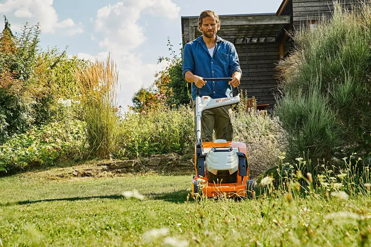 Uomo con tosaerba elettrico in un giardino rigoglioso. Un passo fondamentale per imparare come fare un giardino da zero.