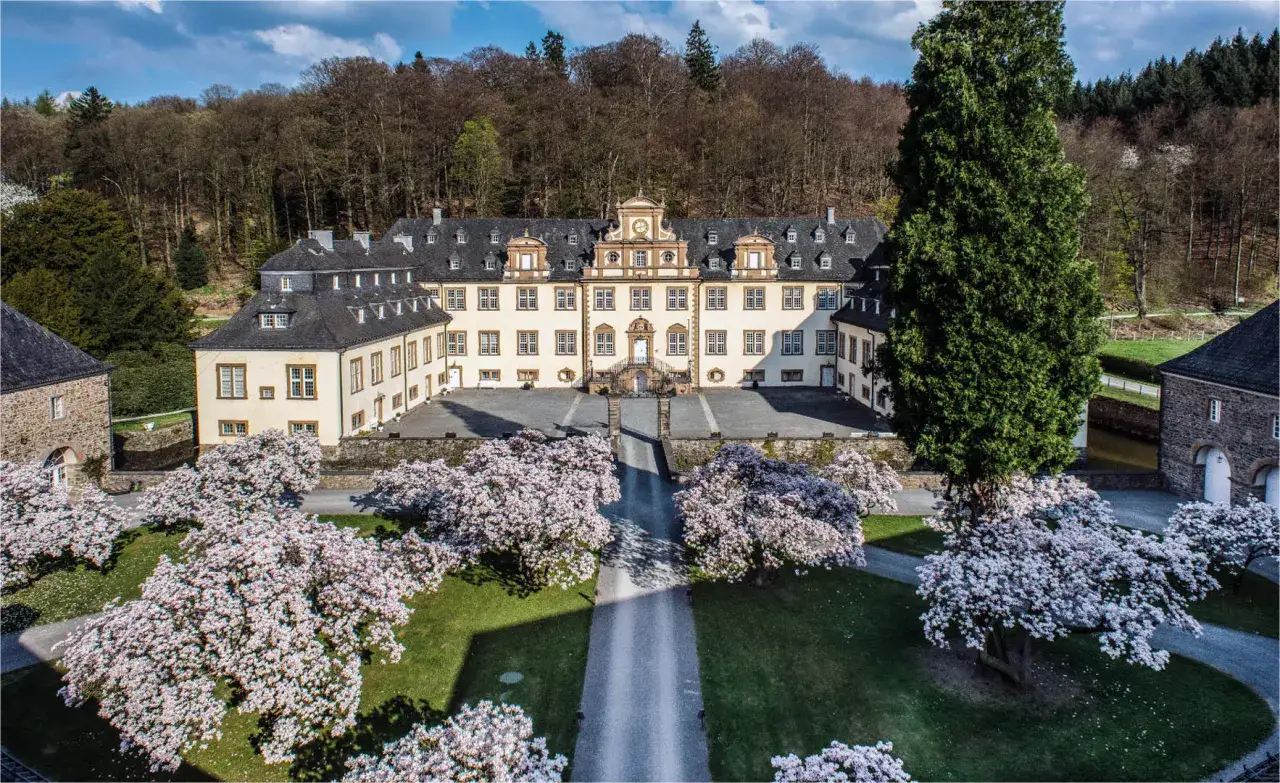 Prachtvolles Schloss Engelskirchen im Fr&uuml;hling, umgeben von bl&uuml;henden Magnolien und alten B&auml;umen.
