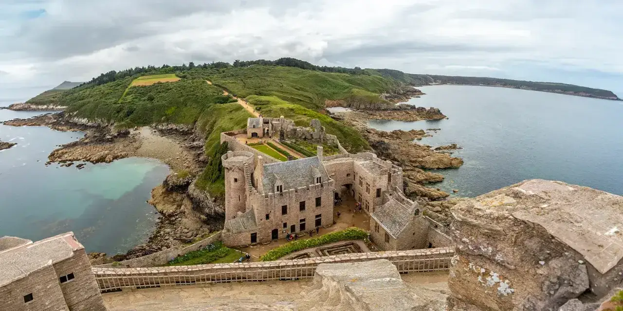 Un château médiéval sur une falaise bretonne, idéal pour savoir où partir en France en mai. La mer d'un bleu profond borde la côte rocheuse.