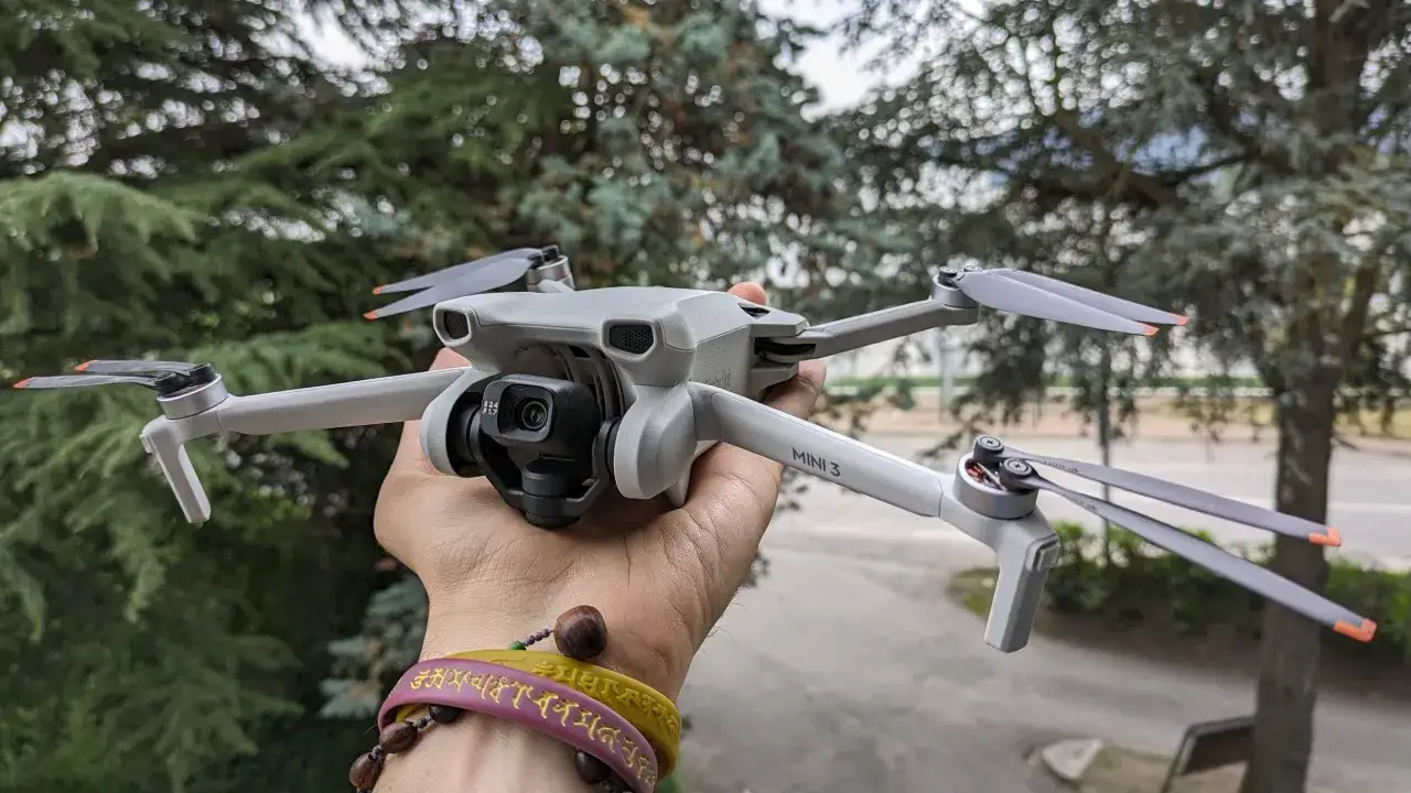 Un drone DJI Mini 3, perfetto per chi cerca un drone DJI senza patentino, tenuto in mano con alberi sullo sfondo.
