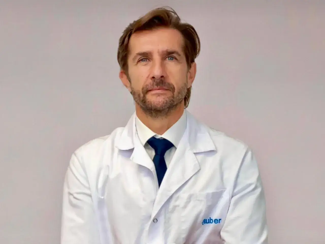 Doctor Miguel S&aacute;nchez Encinas, con bata blanca y corbata azul, mira fijamente.